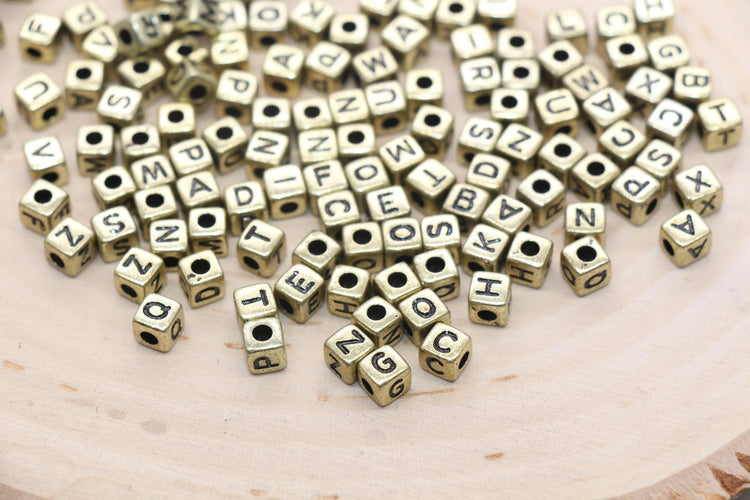 gold cube shaped beads with black lettering on each of them on the smooth wood