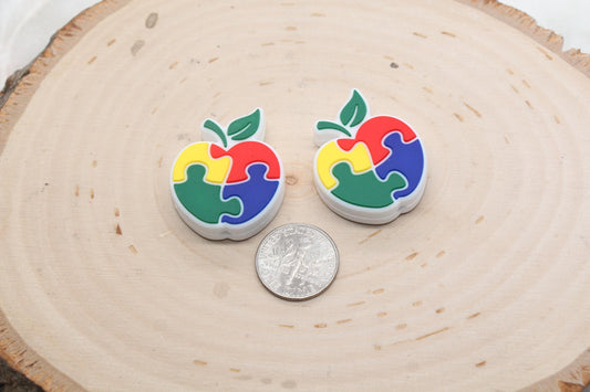 Two colorful apple-shaped pins next to a quarter on a wooden surface.