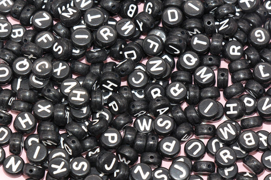 Scattered black alphabet beads with white letters on a pink background.