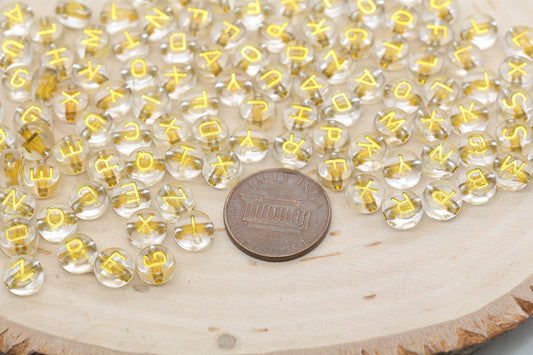 Transparent bead letters scattered around a coin on a wooden surface.