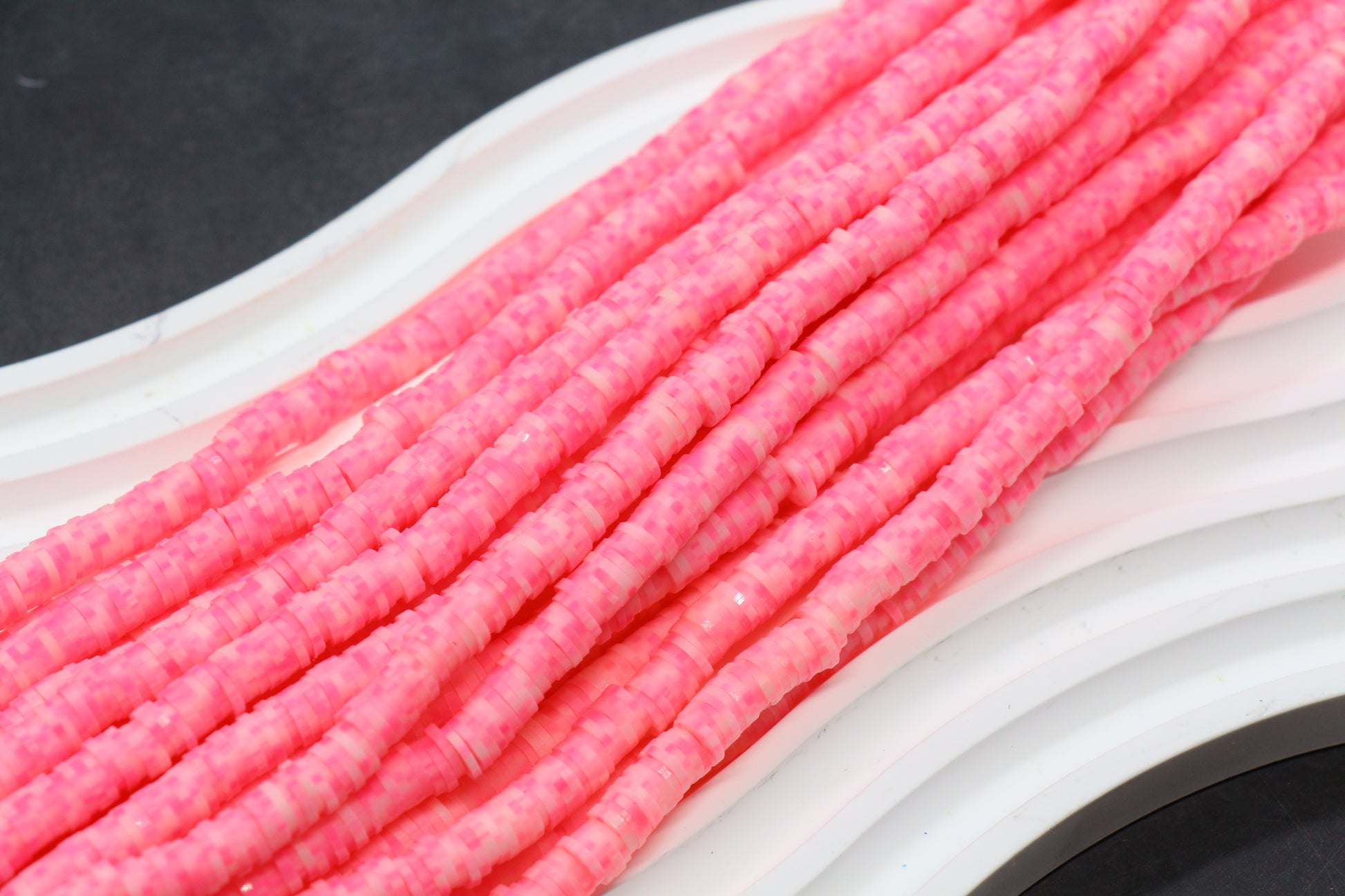 Close-up of pink cylindrical beads on a white surface with a dark background