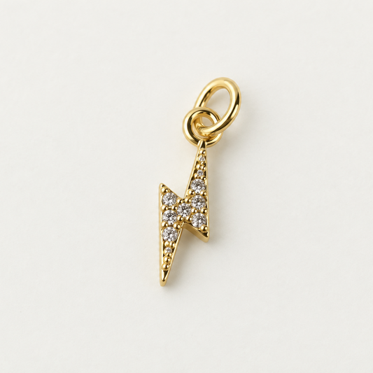 Gold-plated CZ lightning bolt charm on a neutral ivory background