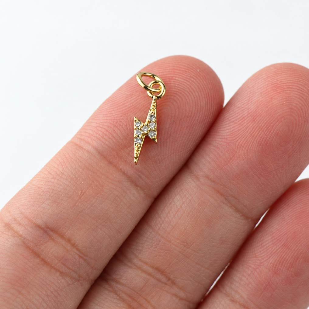 Front of small gold-plated CZ lightning bolt charm resting on fingertips