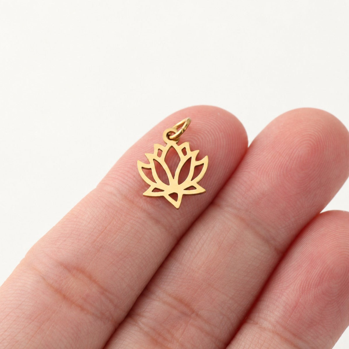Small gold-plated openwork lotus pendant resting on fingertips for scale