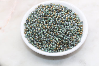 A white bowl filled with small, shiny, greenish-black beads on a marble surface.