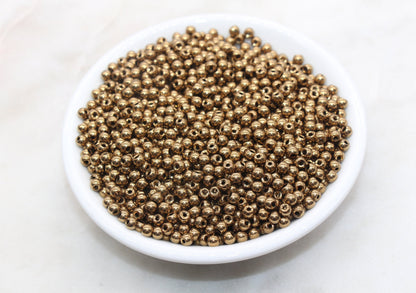 A bowl of small, shiny gold beads on a white surface.