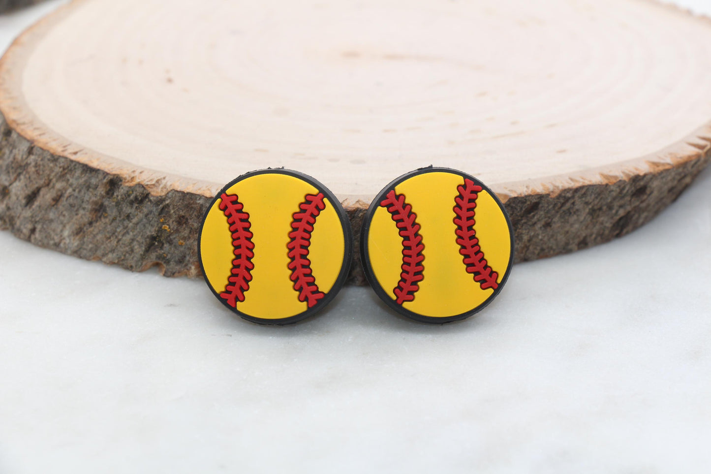 Pair of softball-designed earrings on a wooden slice background.