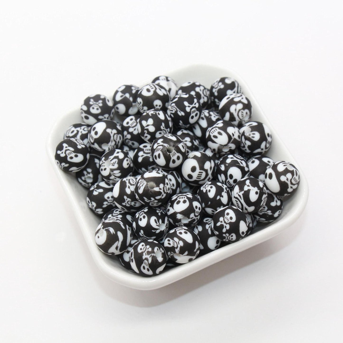 A bowl of black and white, skull-patterned beads on a white background.