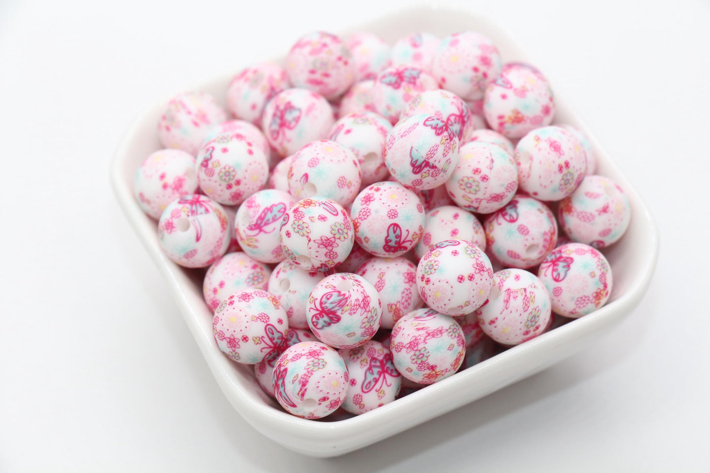 A bowl of pink speckled candies with floral patterns on a white background.